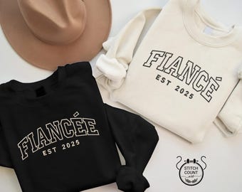 以下が含まれることがあります： 「Fiancé Est 2025」と「Fiancée Est 2025」の文字が大学風のフォントで書かれた、黒と白の2枚のスウェットシャツです。