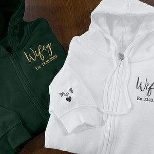 May include: Two zipped hoodies, one green and one white, with the word "Wifey" and the date "Est 13.10.2003" embroidered on them. Both hoodies have a small heart and the initials "Mrs. B" embroidered on the sleeve.