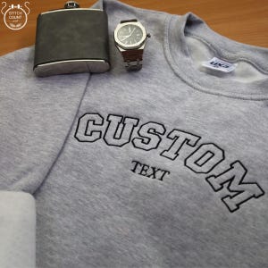 May include: Grey sweatshirt with black embroidered text that reads "CUSTOM TEXT".