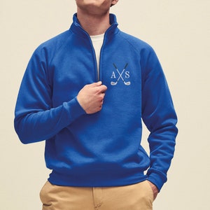 Könnte beinhalten: Royalblauer Quarter-Zip-Sweatshirt mit einem weißen gestickten Monogramm und gekreuzten Golfschlägern.