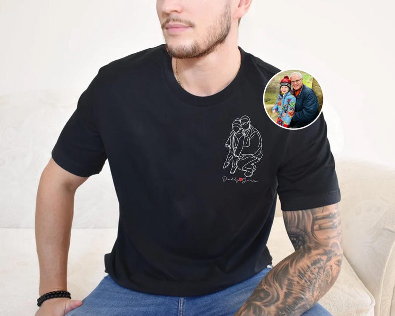 以下が含まれることがあります： 白線画で人物と子供を描いた黒のクルーネックTシャツ。「Daddy Jeans」の文字が筆記体で描かれています。人物と子供の小さな円形画像が右肩にあります。