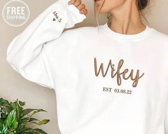 May include: White sweatshirt with the text "Wifey EST 03.08.22" in brown script. The left sleeve has the text "Mrs. S" in brown script with a small heart.