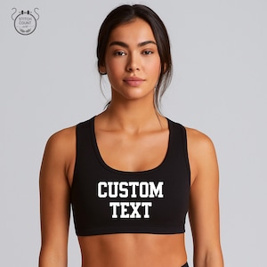May include: Black sports bra with the text "CUSTOM TEXT" in white block letters. The bra has a scoop neckline and is designed for athletic activities. The image shows the bra on a person.