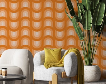 May include: A white armchair with a yellow throw pillow sits in front of a wall with an orange and white geometric pattern. A large green plant is in a brown pot to the right of the chair.
