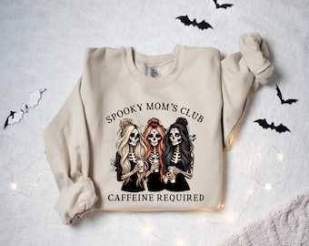 May include: A beige sweatshirt with the text "Spooky Mom's Club Caffeine Required" and a graphic of three skeletons holding coffee cups.