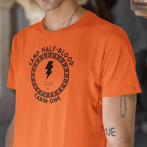 May include: Orange t-shirt with a black graphic of a lightning bolt inside a circle with the text "Camp Half-Blood", "Zeus", and "Cabin One".
