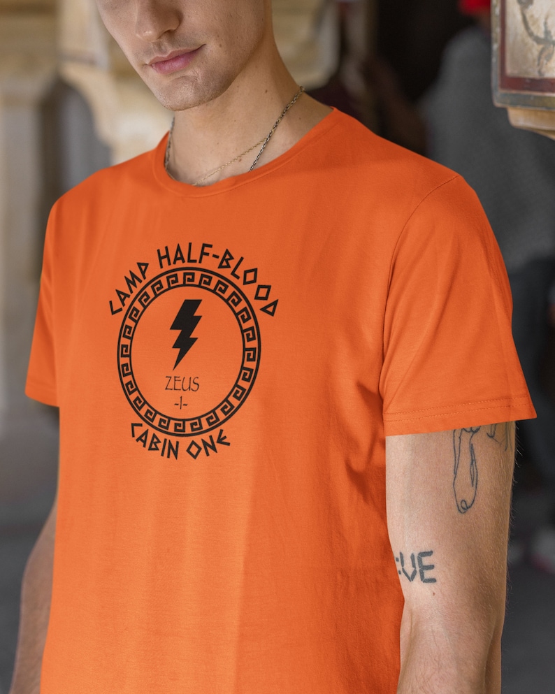 May include: Orange t-shirt with a black graphic of a lightning bolt inside a circle with the text "Camp Half-Blood", "Zeus", and "Cabin One".