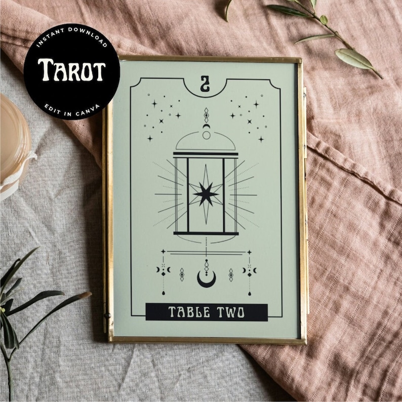 May include: A gold framed print of a tarot card with a light green background. The card depicts a black and white illustration of a lantern with a star inside. The card number "2" and the text "TABLE TWO" are printed in black at the top and bottom of the card.