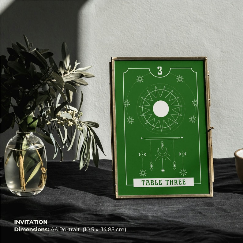 May include: A green invitation card with a gold frame. The card has a white sun design with a white circle in the center. The text "3" and "TABLE THREE" are printed in white on the card.
