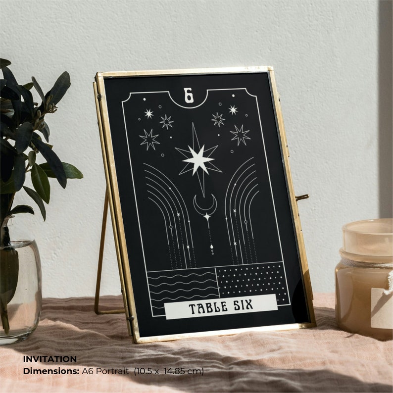 May include: A black and white table number card with a gold frame. The card features a star, crescent moon, and the text "TABLE SIX". The card is 10.5 inches by 14.85 inches.
