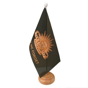 May include: A black desk flag with a gold emblem of the Australian Army and the words "The Australian Army" and "We Forget" on a wooden base.