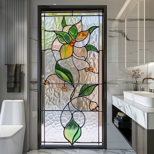 Puede incluir: Una ventana de vidrio emplomado con un diseño floral con una flor blanca con detalles naranjas y hojas verdes. La ventana está enmarcada en negro y está ubicada en un baño.