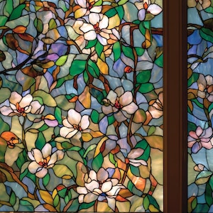 Può includere: Pannello di finestra in vetro colorato con un motivo floreale. Sono raffigurate fiori di magnolia bianchi, foglie verdi e rami marroni. Il vetro è un mosaico di blu, giallo e arancione, incorniciato da un bordo marrone scuro.