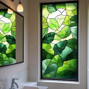 Könnte beinhalten: Ein Buntglasfenster mit einem Blattmuster in verschiedenen Grüntönen. Das Fenster ist schwarz umrahmt und befindet sich wahrscheinlich in einem Badezimmer, mit einem Spiegel und einem Waschbecken. Das Design erinnert an die Natur.