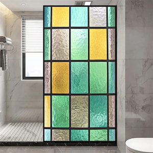 Può includere: Un film per finestre in vetro colorato con un motivo geometrico di quadrati gialli e verdi. Il film è applicato su una finestra del bagno.