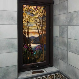 Könnte beinhalten: Ein Buntglasfenster, das eine Landschaft mit einem See, Bergen und Bäumen mit gelben Blüten zeigt. Das Fenster ist in dunklem Holz gerahmt und in eine gekachelte Wand eingefasst.