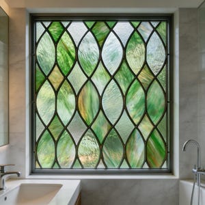 May include: A stained glass window featuring a repeating pattern of green and yellow leaf-like forms. The glass has a textured finish, and the frame is dark. The window is set in a bathroom environment.