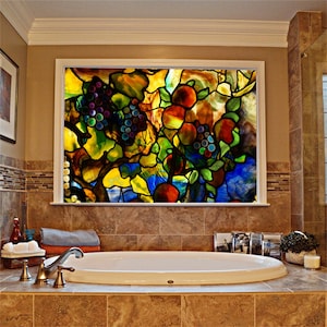 May include: A stained glass window featuring a colourful fruit tree with grapes, oranges, and leaves. The window is situated in a bathroom with a white bath and brown tiles.