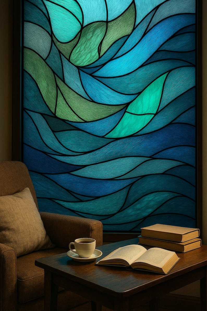 May include: A stained glass window featuring an abstract design in shades of blue and green. A dark frame surrounds the window. In front, a brown armchair, a coffee cup, and books rest on a wooden table.