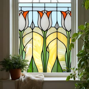 Könnte beinhalten: Buntglasfenster mit einem Blumendesign mit weißen, orangefarbenen und gelben Tulpen. Das Fenster ist schwarz umrandet und vor einem hellblauen Hintergrund platziert. Das Fenster befindet sich in einem weißen Rahmen, mit einer Topfpflanze und einer gefalteten Decke auf der Fensterbank.