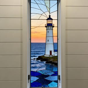 May include: Stained glass window featuring a white lighthouse with a blue and black top, a red door, and a small adjacent building. The scene includes a sunset over the ocean and blue waves. The window is framed in white.