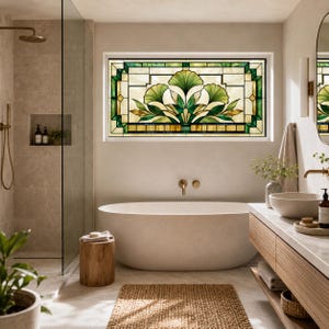 Op de afbeelding: Een rechthoekig glas-in-loodraam met een symmetrisch botanisch ontwerp met groene ginkgo-achtige bladeren en crèmekleurige panelen, omlijst door donkere lijnen, horizontaal geplaatst boven een wit ovaal bad in een badkamer.