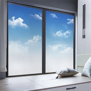 May include: A frosted window film with a cloudy sky and white clouds design. The film is installed on a window in a room with a white wall and a white window sill.