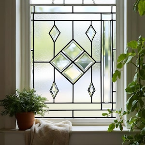 Könnte beinhalten: Ein dekoratives Fenster mit einem schwarzen Gittermuster und rautenförmigen Glasscheiben. Das Fenster ist in einem weißen Rahmen eingefasst und befindet sich vor einer Fensterbank mit einer Topfpflanze und einer gefalteten Decke.