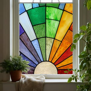 Può includere: Una colorata vetrata con un disegno a raggiera. La finestra presenta uno spettro di colori, tra cui verde, blu, viola, arancione e rosso, disposti a semicerchio. La finestra è incorniciata in bianco.