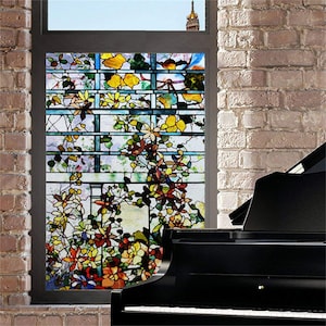 May include: A stained glass window film featuring a colourful floral design with a trellis pattern. The film is applied to a window in a brick wall, with a black grand piano in the foreground.