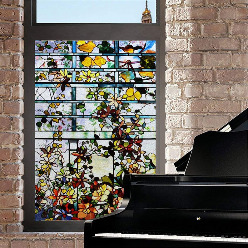 May include: A stained glass window film featuring a colourful floral design with a trellis pattern. The film is applied to a window in a brick wall, with a black grand piano in the foreground.