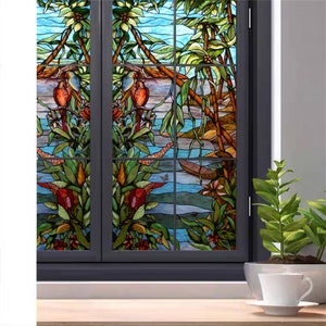 May include: A stained glass window film depicting a tropical scene with palm trees, birds, and a river. The film is designed to add privacy and style to any window.