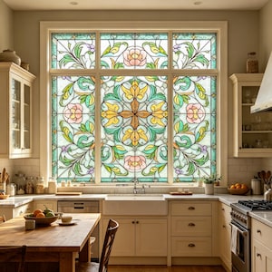 Puede incluir: Una cocina con una gran ventana de vidrieras ornamentada como punto focal. La ventana presenta un diseño floral con tonos rosas, amarillos, verdes y morados. La cocina tiene gabinetes de color claro, una mesa de madera y un fregadero blanco.