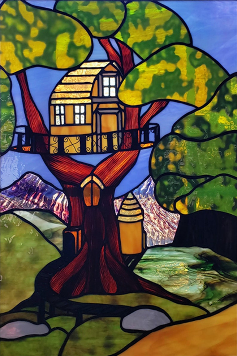 May include: A stained glass window featuring a tree house nestled in a large tree with a brown trunk and green foliage. The tree house is yellow with brown detailing and has two windows. The background shows a blue sky with mountains and a river.