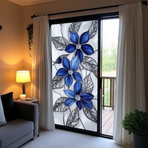 May include: A decorative window film showing three large blue flowers with crystal centres and detailed silver leaves. The design is set against a white background with black outlines, creating a stained-glass effect. The film is applied to a sliding glass door.