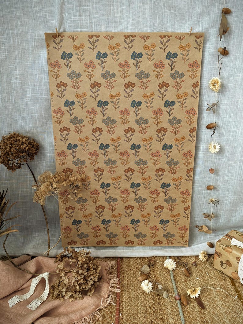 Puede incluir: Una hoja rectangular de papel de regalo color canela con un patr&oacute;n repetitivo de peque&ntilde;as flores estilizadas en tonos naranja apagado, azul polvoriento y rosa suave. El dise&ntilde;o floral est&aacute; dispuesto en filas verticales por todo el papel.