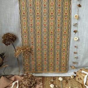 Puede incluir: Una l&aacute;mina de papel rectangular con un patr&oacute;n repetitivo de l&iacute;neas onduladas verticales en azul oscuro y verde oliva, intercaladas con peque&ntilde;os motivos florales estilizados en tonos coral, azul claro y rosa suave sobre fondo beige.