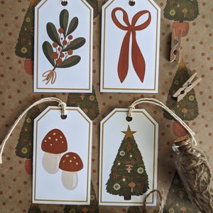 May include: Four illustrated gift tags with a gold border. The tags feature a sprig of holly, a red bow, a pair of mushrooms, and a decorated Christmas tree.