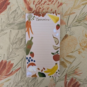 May include: A notepad with the word "Groceries" in cursive script at the top. The notepad is decorated with illustrations of carrots, cheese, strawberries, garlic, pears, apples, bananas, and other produce. The notepad has lined pages.