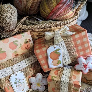 May include: A stack of wrapped presents with orange and white patterned paper, hessian ribbon, and lace trim. The gifts are decorated with small fabric flowers and tags. The presents are sitting on a crocheted doily.