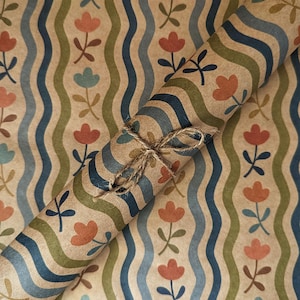 Puede incluir: Un rollo de papel de regalo kraft marr&oacute;n con un patr&oacute;n repetitivo de l&iacute;neas onduladas verticales en azul oscuro y verde oliva, intercaladas con peque&ntilde;as flores naranjas y azul claro, atado con un fino cordel de yute natural.