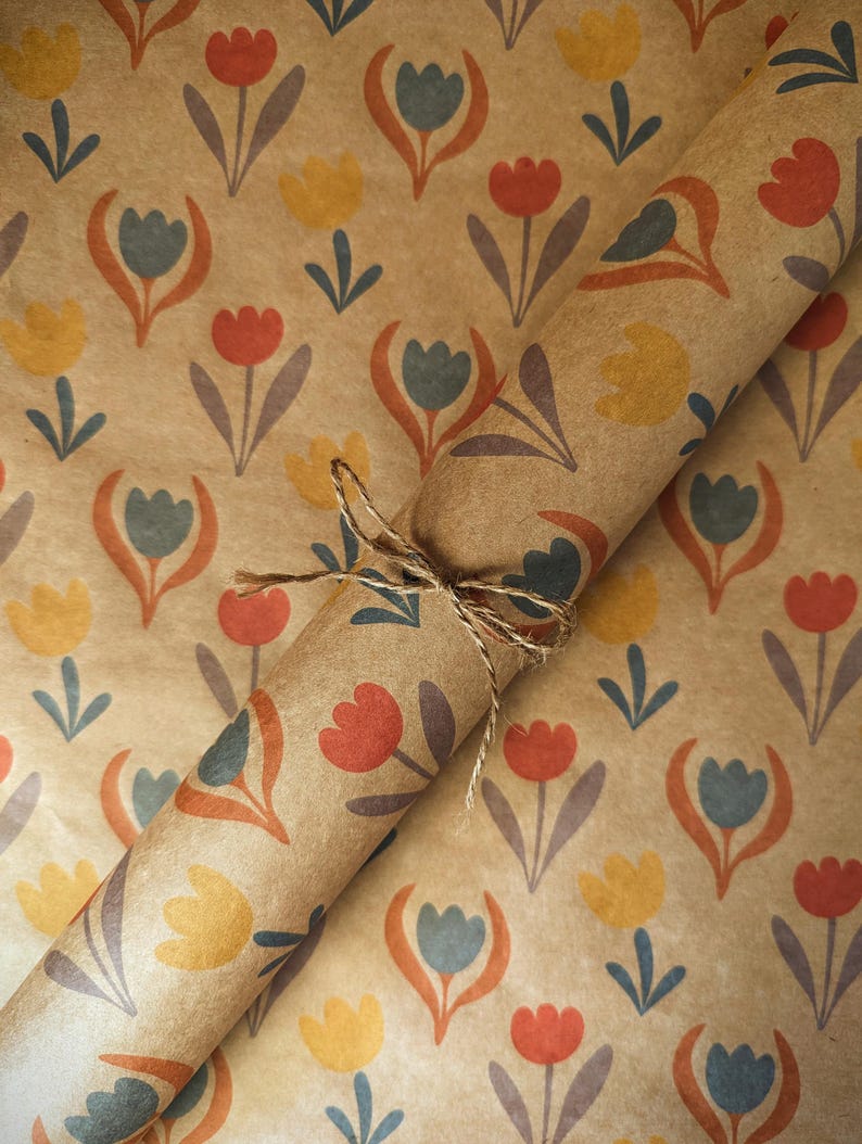 Puede incluir: Un rollo de papel de regalo kraft marr&oacute;n con un patr&oacute;n repetitivo de tulipanes estilizados en tonos rojo, amarillo y azul apagado. El papel est&aacute; atado con un trozo fino de cuerda de yute natural envuelto alrededor del centro del rollo.