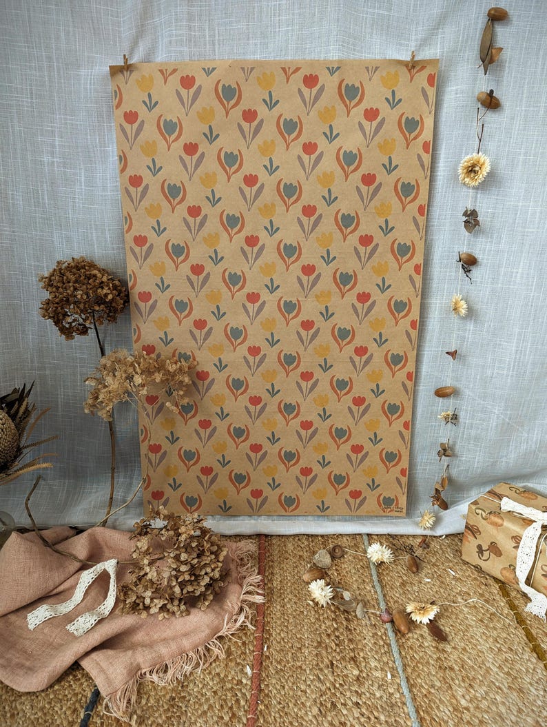 Puede incluir: Una hoja rectangular de papel kraft marr&oacute;n con un patr&oacute;n repetitivo de tulipanes estilizados en tonos rojo, amarillo y azul gris&aacute;ceo apagado. El papel se muestra verticalmente, exhibiendo un estampado floral consistente en toda su superficie.