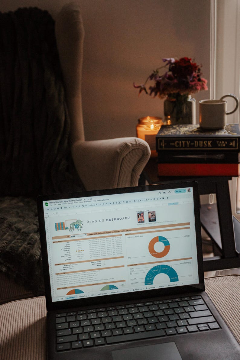 May include: A laptop displaying a "Reading Dashboard" spreadsheet with charts and data. The laptop is open on a couch, near a chair, books, a candle, and a mug. The screen shows data visualization.