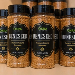 May include: Clear plastic spice jars filled with brown ground beneseed. Each jar features a black label with the text Okra Pantry, Beneseed, Premium Ground Beneseed, and Net Wt. 5 oz (142g). The jars have black screw-on lids and are arranged in a group.