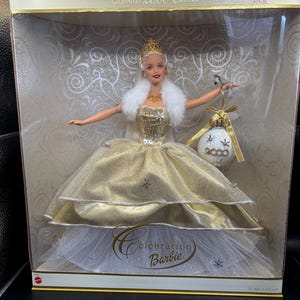 May include: A Special 2000 Edition Celebration Barbie doll in a clear display box. The doll wears a gold gown with a white fur stole and a gold crown. She holds a Christmas ornament. The box has the text "Celebration Barbie".