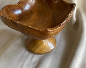 May include: A wooden bowl with a fluted rim and a pedestal base. The bowl is made of dark brown wood and has a natural finish.