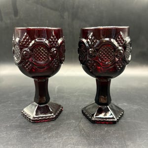 Puede incluir: Dos copas de color rojo rubí con diseños en relieve. Las copas presentan un patrón de diamantes y están sostenidas por un tallo y una base hexagonal. El vidrio tiene un acabado brillante.