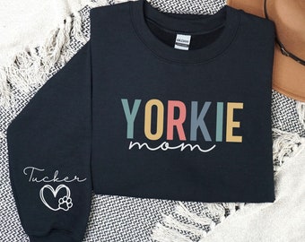 May include: Black sweatshirt with the text "YORKIE mom" in rainbow colors. The left sleeve has the text "Tucker" with a heart and paw print.