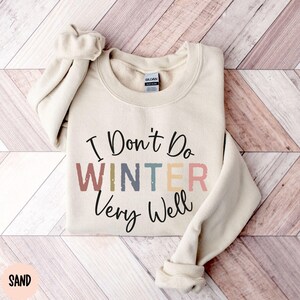 May include: A beige sweatshirt with the text "I Don't Do Winter Very Well" in colorful, distressed lettering.